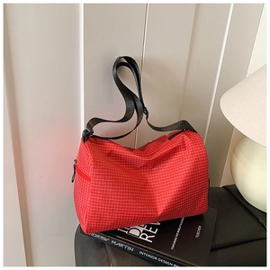 Detail view of red plaid cylinder bag on books with adjustable strap and zip closure