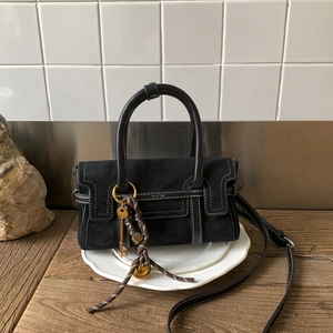 Detail of black suede and leather bag with white contrast stitching and key charm