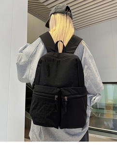 Rear view of a black nylon multi-pocket backpack worn by a model in an urban setting