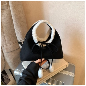 Détail d'un sac à main en daim noir mat avec garniture en laine d'agneau et nœud à pompons