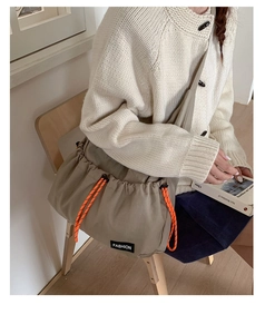 Detail showing khaki drawstring crossbody bag with orange woven rope and fashion label