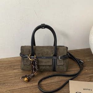 Detail of olive green suede handbag with white contrast stitching and woven charm