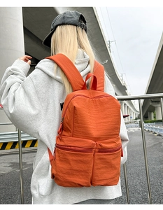 Detail of bright orange nylon backpack with two front pockets shown in outdoor city setting
