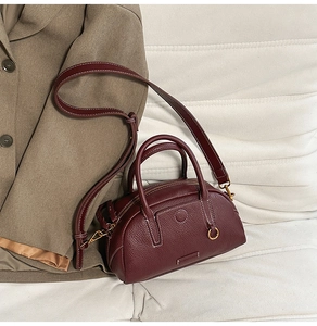 Close-up of burgundy lychee grain leather boston bag with white contrast stitching details