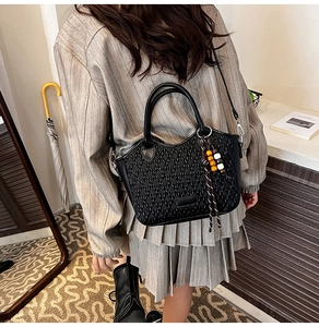 Detail of black woven bucket bag with wooden bead charm on a model in home setting