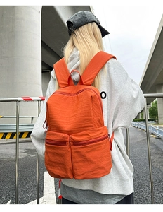 Rear view of a model wearing a large orange nylon backpack with dual front zipper pockets