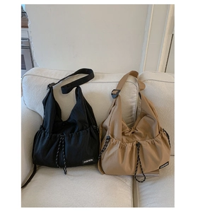 Detail view of black and khaki nylon crossbody bags with drawstrings on a soft white sofa