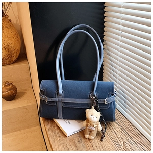 Détail du sac Boston en denim bleu avec sangle décorative et pendentif ours de mode