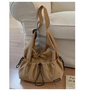 Close-up of khaki drawstring crossbody bag showing side pleats and fashion label on sofa
