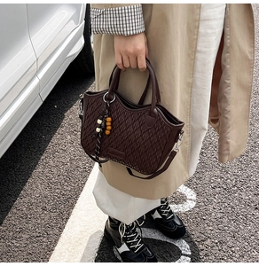 Detail of dark brown woven texture bucket bag with wooden bead charm in a street setting