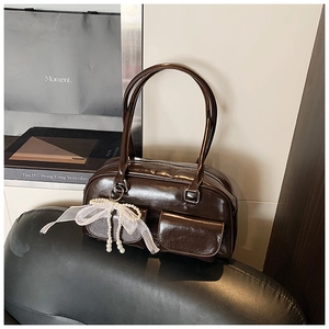 Detail of dark brown glossy underarm bag with lace pearl bow charm and dual handles