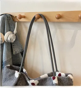 Detail of grey knitted tote bag with floral accents hanging in a cozy lifestyle setting