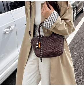 Detail of dark brown woven bucket bag featuring a decorative beaded charm and crossbody strap