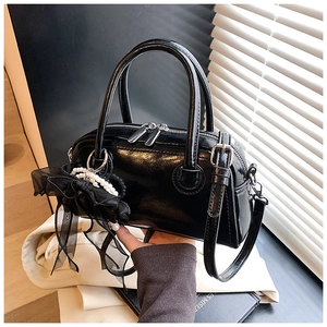 Gros plan détaillé d'un sac Boston en cuir verni noir avec charme en dentelle perlée