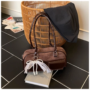 Detail of brown suede shoulder bag with glossy trim and a pearl bow charm accessory