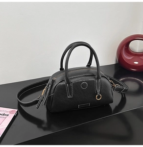 Detail view of black lychee leather bowling bag with white contrast stitching and gold D-rings