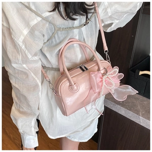 Détail d'un sac Boston rose brillant avec nœud en organza et breloque en perles élégante