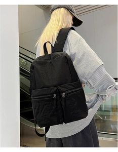 Close-up of lightweight black nylon backpack showing dual front zipper pockets on a model