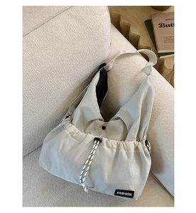 Detail of beige nylon crossbody bag with drawstring design and fashion label on a sofa