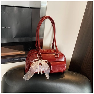 Detail of red glossy shoulder bag with lace pearl bow charm and dual front pockets