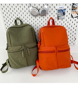 Detail of dual front zipper pockets on nylon backpacks in olive green and bright orange