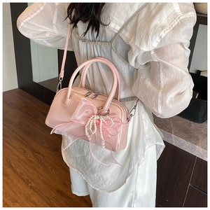 Sac polochon rose brillant avec nœud en organza et perles porté par un modèle