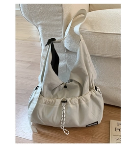 Detail view of large cream canvas crossbody bag with drawstring closure and fashion tag