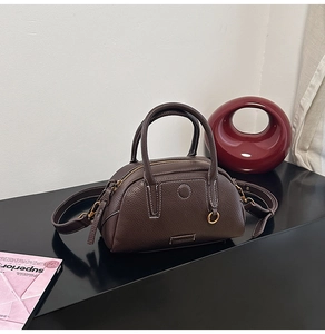 Close-up of dark brown pebble leather bowling bag with white stitching and gold hardware