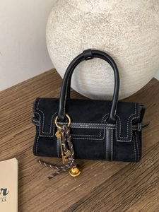 Fashionable black suede handbag with contrast white stitching and decorative gold charms