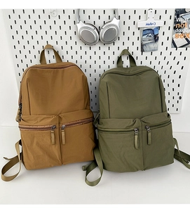 Detail view of water-resistant nylon backpacks in brown and olive with dual front pockets