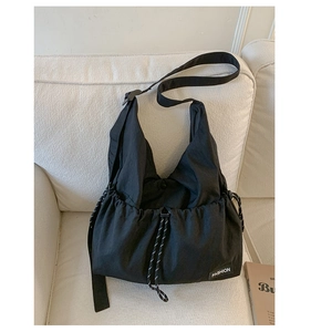 Detail view of black nylon drawstring crossbody bag with fashion label on white sofa