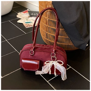 Close-up of burgundy velvet underarm bag with glossy patent leather and pearl bow charm
