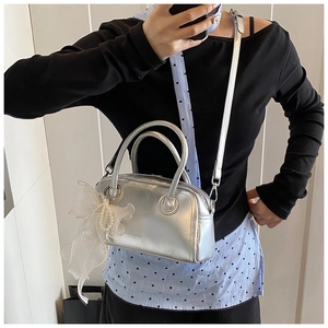 Détail d'un sac à main argenté avec nœud en dentelle, breloque perle et poignées rondes