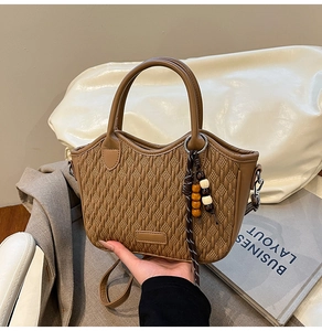 Detail shot of caramel brown woven bucket bag with wood bead tassel and leather handle