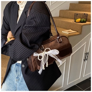 Detailed close-up of dark brown suede boston bag with decorative pearl bow charm