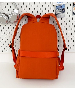Detail view of orange backpack showing padded shoulder straps and suitcase luggage strap