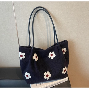 Close-up of navy blue felt tote bag with white daisy embroidery on a leather surface
