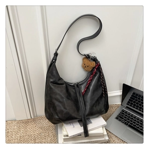 Détail du sac hobo noir en cuir avec zips à pompons et charm d'ours sur des livres
