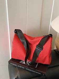 Red plaid crossbody pillow bag with adjustable black strap on a minimalist studio setting
