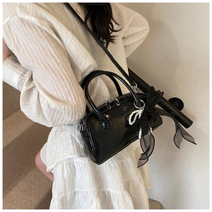 Détail du sac bowling en cuir verni noir avec nœud en tulle et breloques en perles