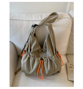 Detail of khaki hobo bag featuring vibrant orange drawstrings and a black fashion label