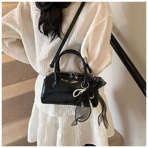 Détail du sac à main noir brillant avec nœud en tulle et breloque perle élégante