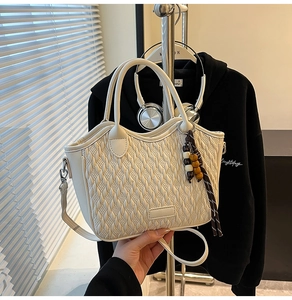 Close-up of cream woven bucket bag with beaded charm and adjustable crossbody strap