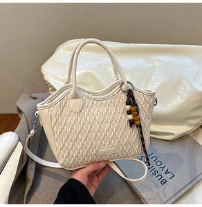 Detail of woven texture white bucket bag with circular handle and wooden bead charm