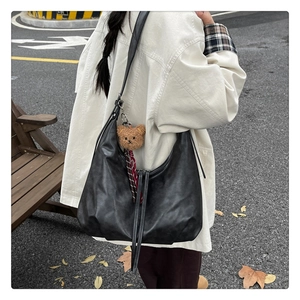 Détail du sac hobo en cuir noir avec un joli pendentif ours en peluche marron en ville