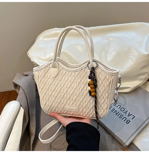Detail of white woven bucket bag featuring beaded tassel charm and faux leather texture