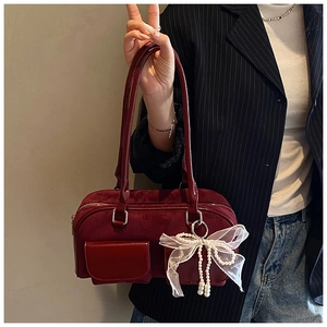 Detail of burgundy suede shoulder bag with lace bow and pearl pendant on model