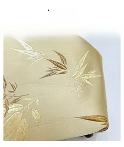 Detail view of gold silk satin fabric with elegant bamboo leaf embroidery and fine stitching
