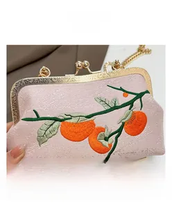 Détail du sac brodé rose avec motifs de kakis orange et une chaîne dorée