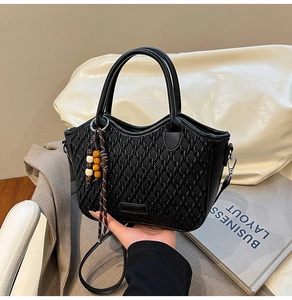 Detail of black pleated quilted bucket bag with woven texture and beaded tassel charm